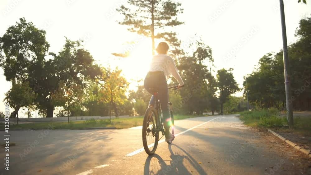 back view woman riding a bicycle through the park in sunlight