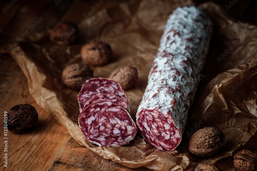 Italian salami with walnuts on craft paper on rustic wooden background. Italian salami with walnuts on craft paper on rustic wooden background.