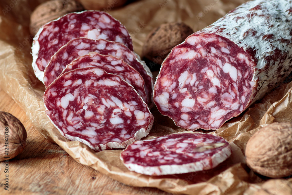Italian salami with walnuts on craft paper on rustic wooden background. Italian salami with walnuts on craft paper on rustic wooden background.
