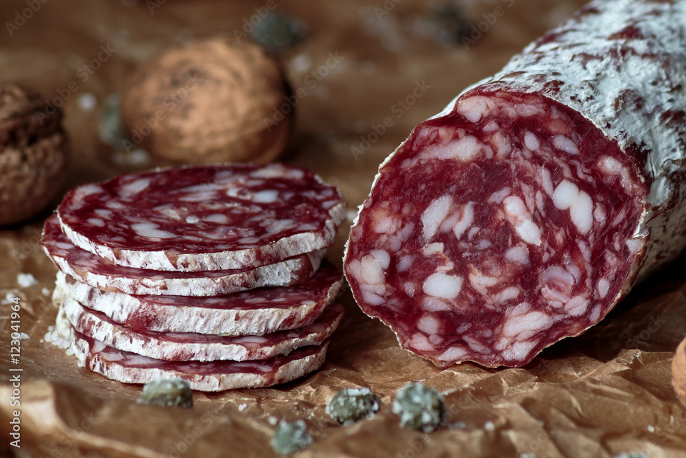 Italian salami with walnuts on craft paper on rustic wooden background. Italian salami with walnuts on craft paper on rustic wooden background.