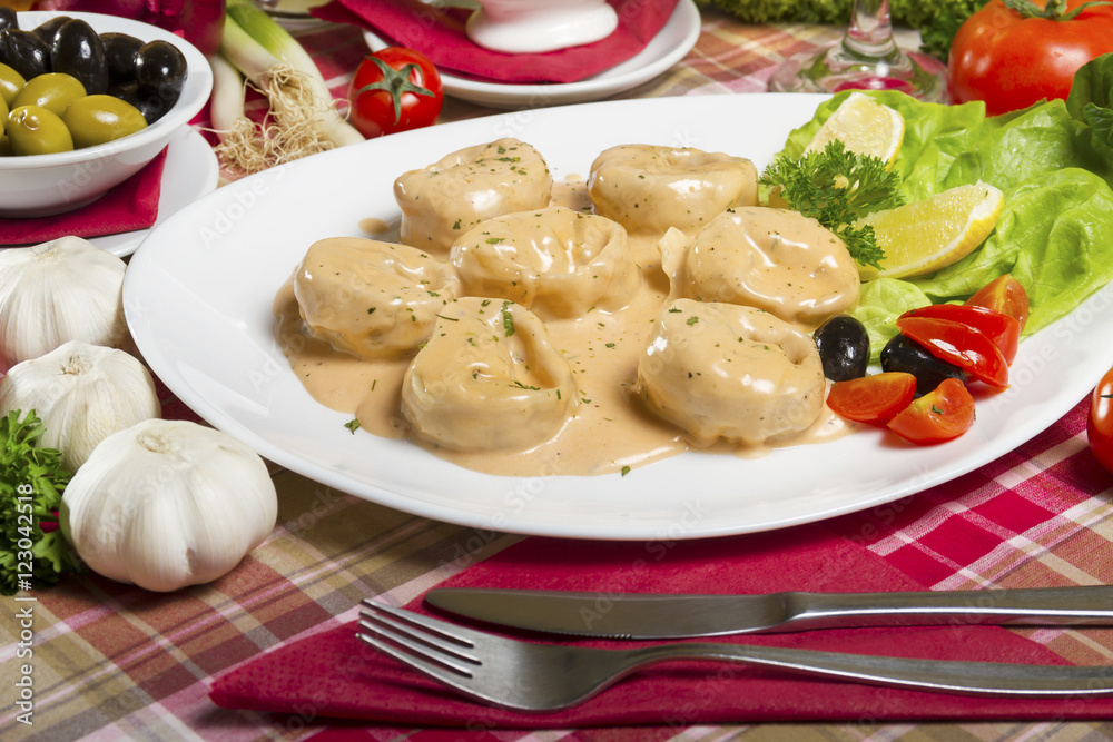 Salmon tortellini in sauce served on a white plate with lemon, olives, cherry tomatoes and parsley next to fresh garlic. Salmon tortellini in sauce served on a white plate with lemon, olives, cherry tomatoes and parsley next to fresh garlic.