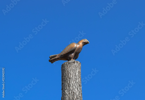 Figurine of a falcon on a stump of a tree against the blue sky. Figures of animals made of wood. Woodcarving