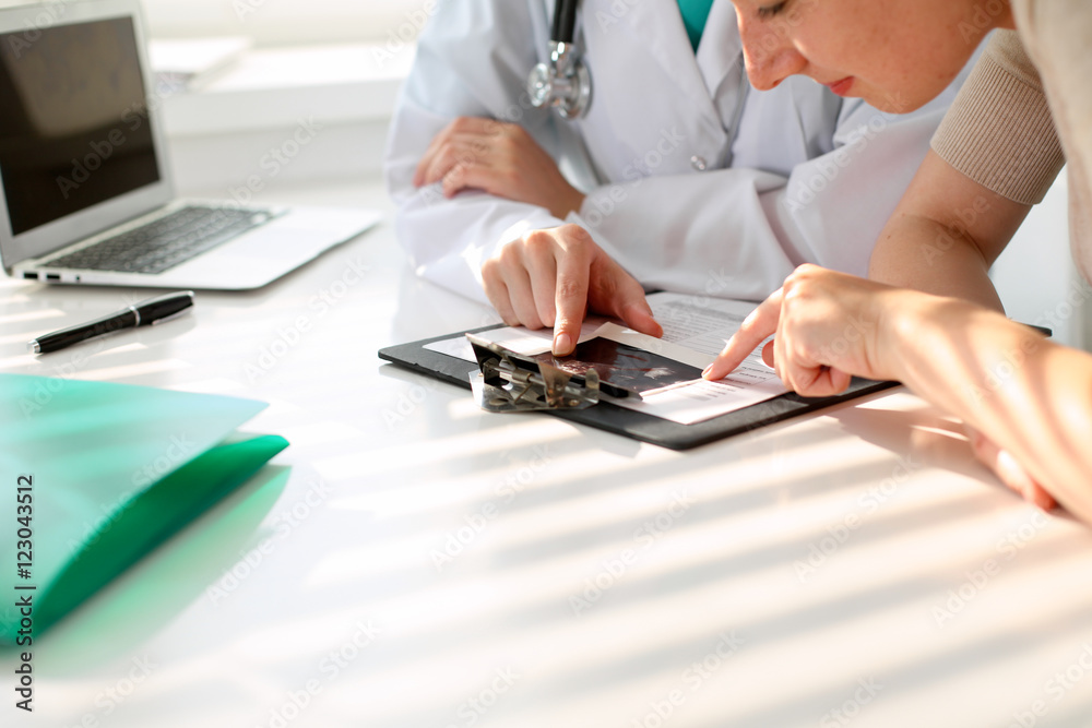 Doctor pointing into medical history form and discussing something with her patient. Close-up. Doctor pointing into medical history form and discussing something with her patient. Close-up.