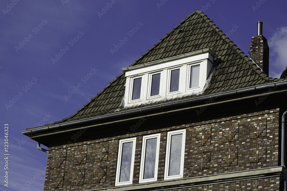 Wohnhaus mit schwarzen Klinkern und einer Dachgaube vor blauem Himmel