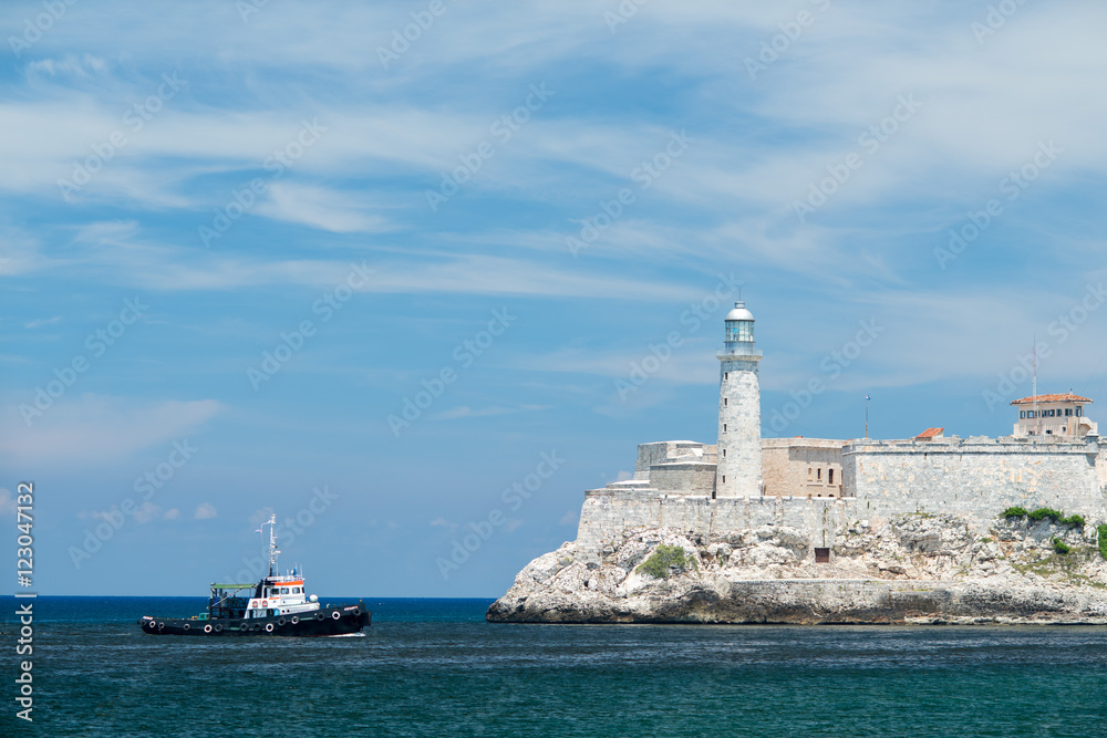 Small ship is floating in the Atlantic Ocean. Lighthouse on a fortress is near an entrance to Havana bay at summer sunny day. Small ship is floating in the Atlantic Ocean. Lighthouse on a fortress is near an entrance to Havana bay at summer sunny day.