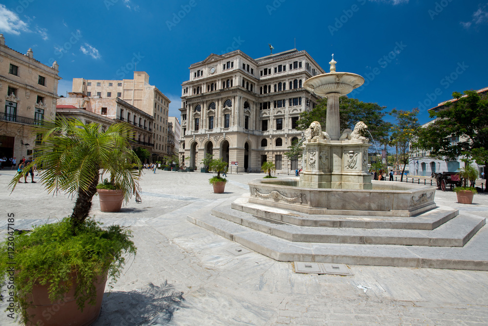 Panoramic view to main square San Francisco in Havana at summer sunny day. Fountain with sculptures, architecture of ancient high buildings and small streets of capital.