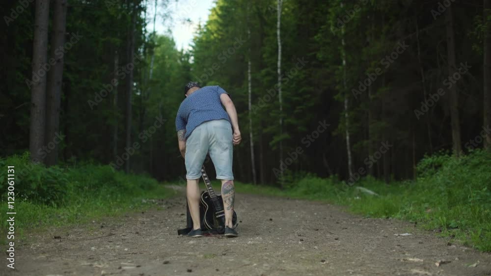 Man is playing at the electric guitar in forest