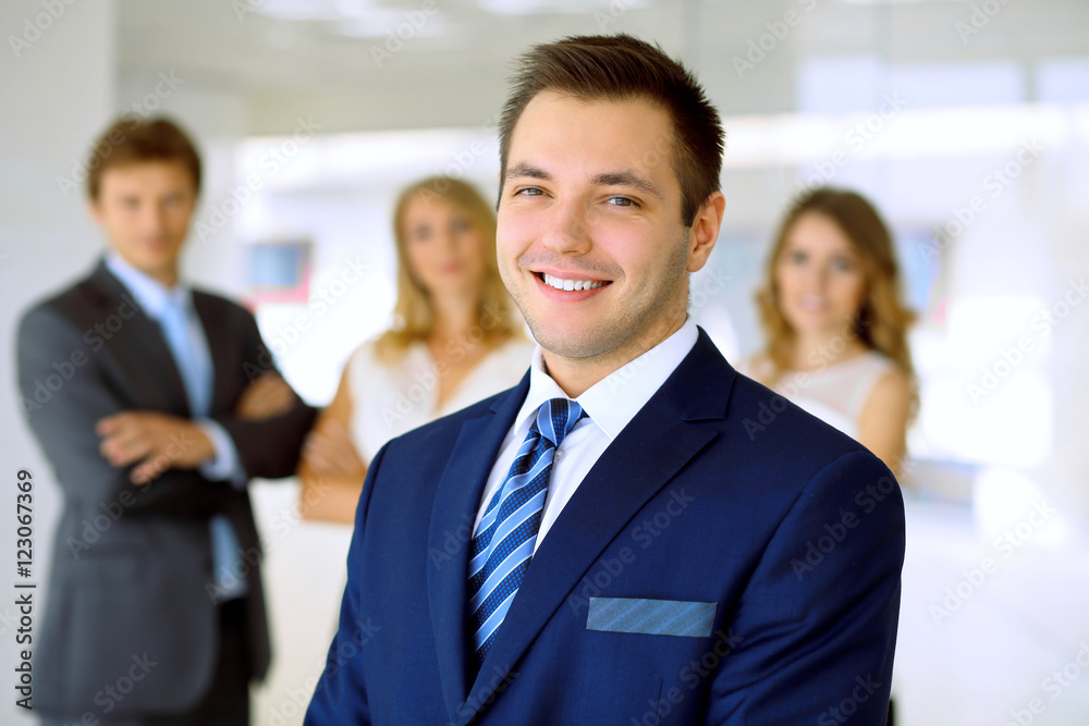 Smiling businessman in office with colleagues in the background Smiling businessman in office with colleagues in the background
