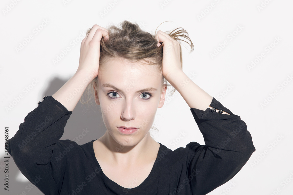 Young blonde woman keeping apart her hair from her face with hands, looking to camera, over a white background. Young blonde woman keeping apart her hair from her face with hands, looking to camera, over a white background.