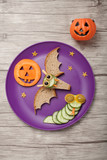 Halloween bat and snake made of bread and cucumber on plate and board