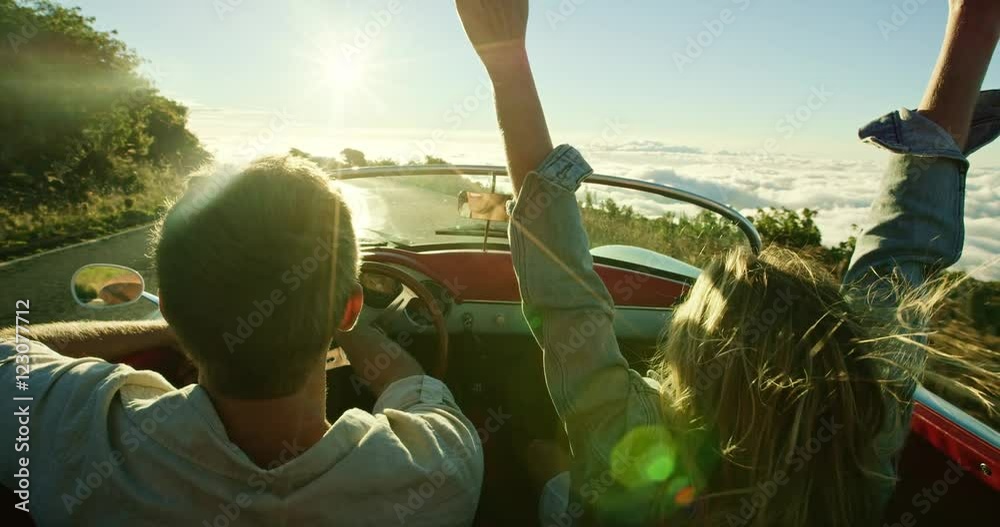 Happy couple driving on country road into the sunset in classic vintage sports car
