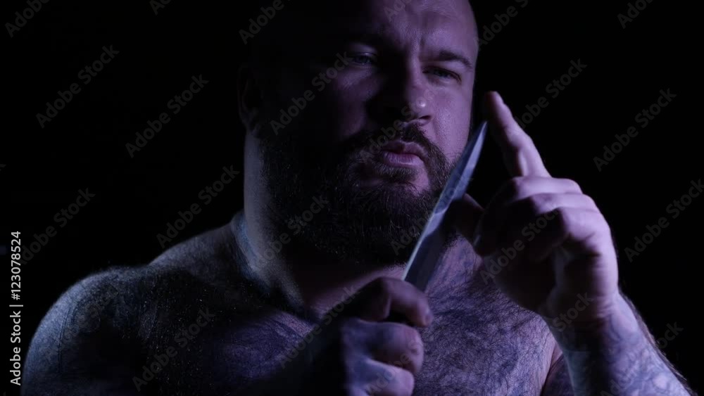 Bald tattoed bearded muscular gangster with a knife. 4K UHD