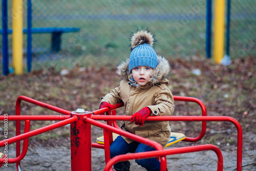 Fototapeta Naklejka Na Ścianę i Meble -  Cute little boy sitting on roundabout at playground