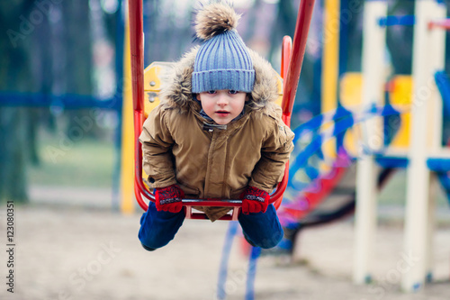 Cute little boy riding on swing in park and looking at camera