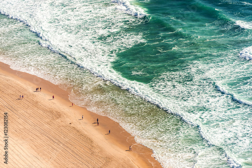Aerial view from above of ocean, sea beach and water waves with people on sand shore with emphasis of the scale of people and nature. Surfers Paradise, Gold Coast, Queensland Australia
