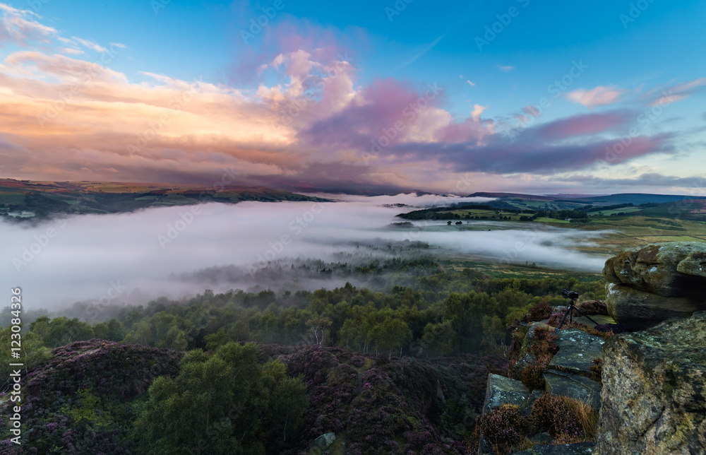 Fototapeta Colorful Surise Clouds over Valley Covered in Mist with Photography Camera on the Edge of Rocks