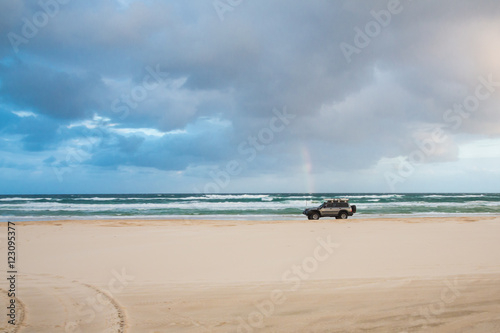 Lonely car passes rainbow at sunset on Fraser Island coast