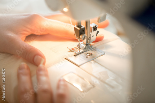 Hands at sewing machine holding some fabric, view over the shoulder, close-up, closeup