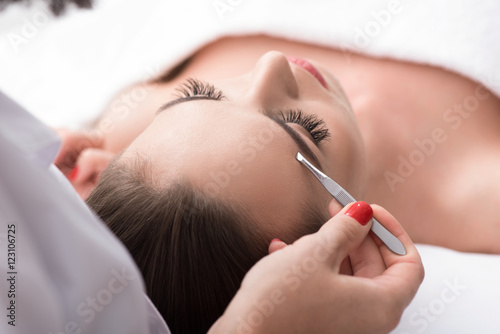 Professional beautician tweezing human brows