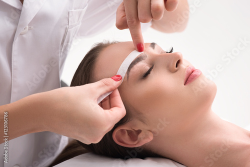 Experienced cosmetician pulling out brows