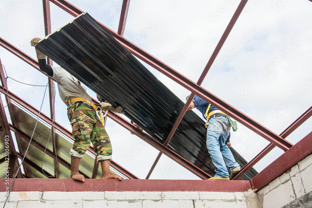 Naklejka premium Roofing construction workers install metal sheet on the roof.