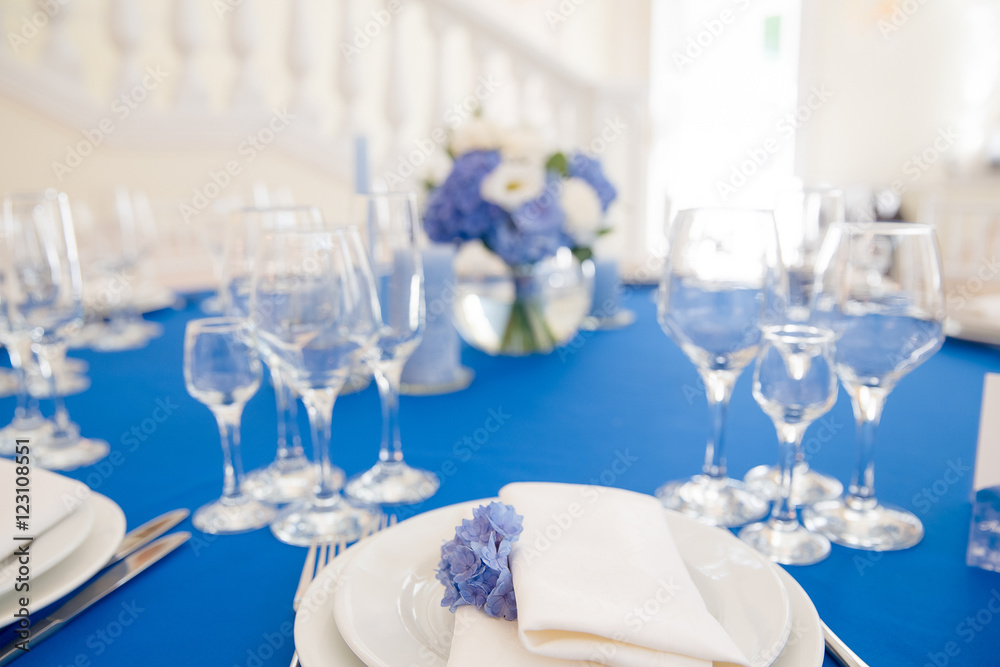 White dinner plates stand on a table covered with blue cloth