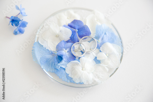 Silver wedding rings lie on the petals of blue and white flowers