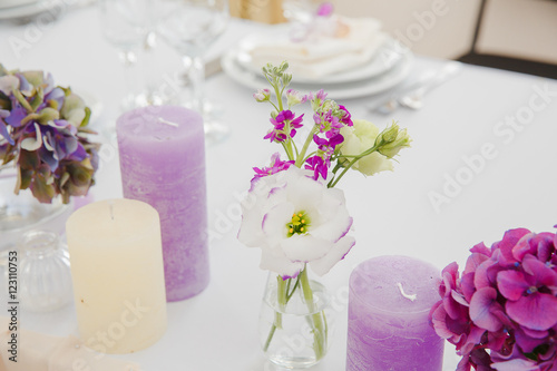 Dinner table deocration. White and violet flowers in glasses wit