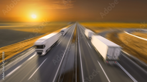 Four trucks in motion blur on the empty highway at sunset