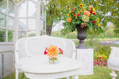 A little bouquet stands on the white table before a white garden