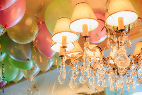 Rich chandelier hangs under a wall full of colored balloons