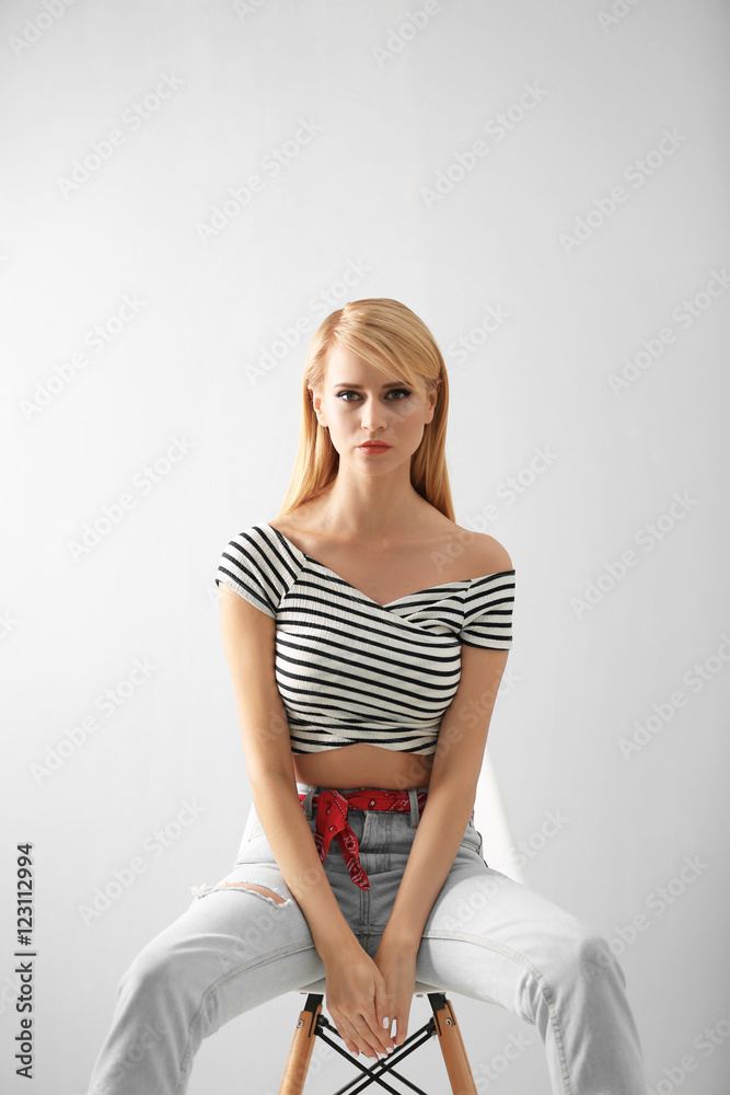 Naklejka premium Pretty young woman in casual clothes sitting on chair against light background