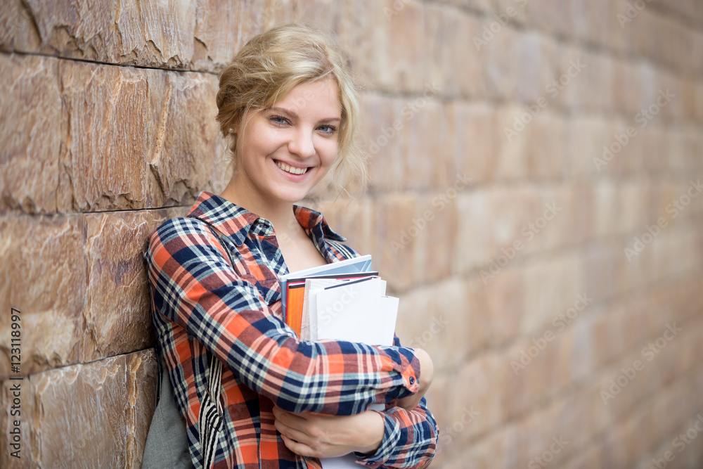 Portrait of a smiling attractive student with books against the brick wall. Back to school concept photo