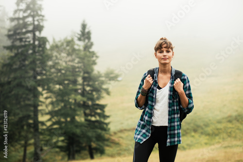 happy traveler women with backpack somewhere in the mountains with fog and trees behind photo