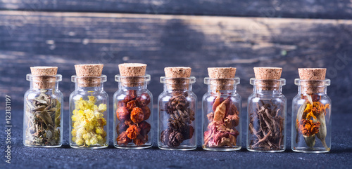 Tablou pe pânză Herbs in bottles on wooden background