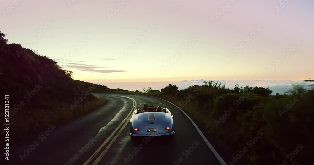 Happy couple driving on country road into the sunset in classic vintage ...