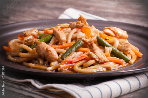 Noodles with chicken and vegetables on a dark plate and a linen