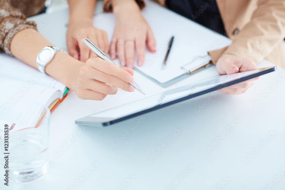 Two business women in a meeting discussing information on a tablet-pc. Close up view of their hands. Two business women in a meeting discussing information on a tablet-pc. Close up view of their hands.