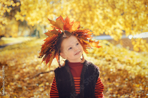Little girl with wreath of maple leaves standing in the autumn