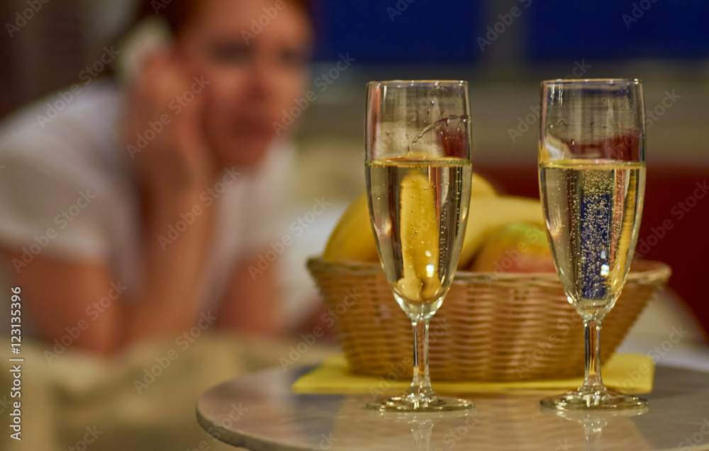 Two glasses of sparkling wine in hotel room with woman in backgr