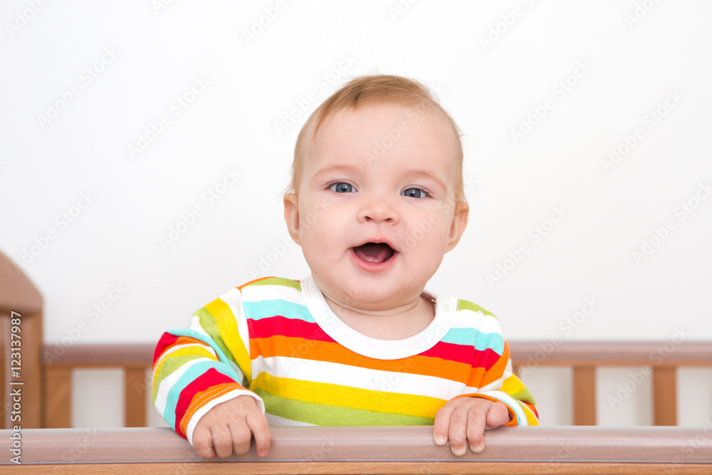 A baby is smiling in the crib and holds onto the side of the bed
A baby is smiling in the crib and holds onto the side of the bed