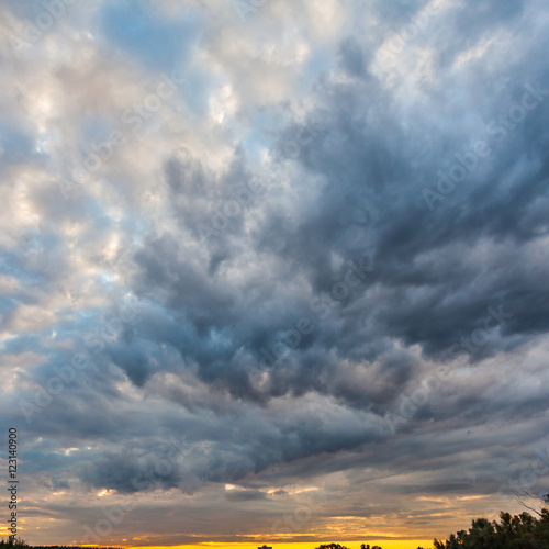 Beautiful dramatic sky with gray clouds and sunset. Dark blue feather shaped clouds in the background of bright orange sunset.