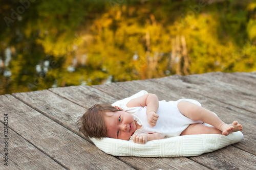 Baby lying on the blanket on pier hext to the river