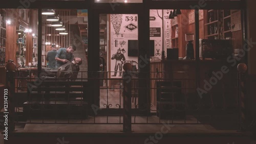 Vintage barbershop exterior HD video. Barber working with client beard. View from street through panoramic glass window entrance to retro hairdressing salon interior
