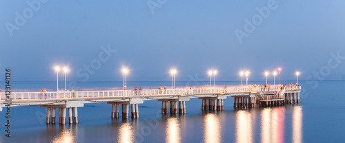 Molo di Marina di Massa in Toscana durante il tramonto con luci che si riflettono sul mare calmo sotto al ponte d'estate. photo