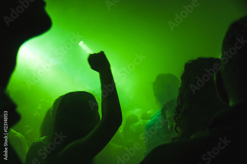 Serata in discoteca con gente che balla con le mani e pugni alzati dietro a neon e led verdi e nebbia photo