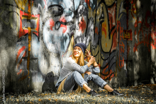 Fashionable girl with long blond hair in stylish clothes standing on a background of graffiti © puhimec