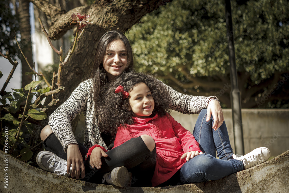 Niña y adolescente, hermanas felices sentadas juntas en el parque.