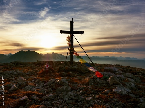 Big wooden cross at mountain peak in wind with Buddhist praying flags. Cross on top of Alp peak