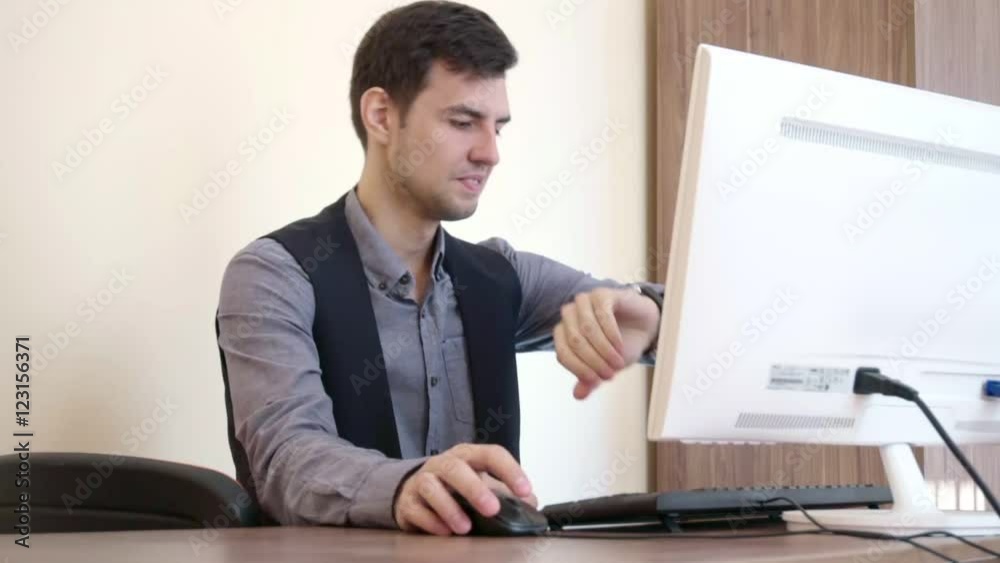 Tired man working at the computer, look at his watch and leave Tired man working at the computer, look at his watch and leave